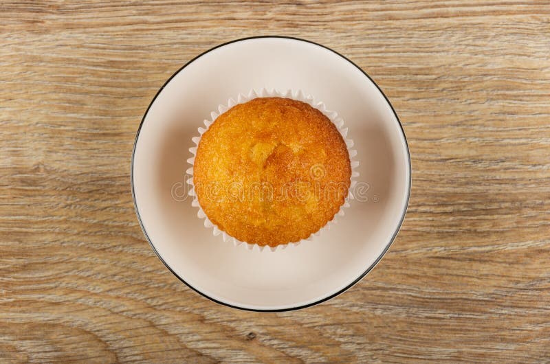 Muffin in wrapper in white bowl on wooden table. Top view