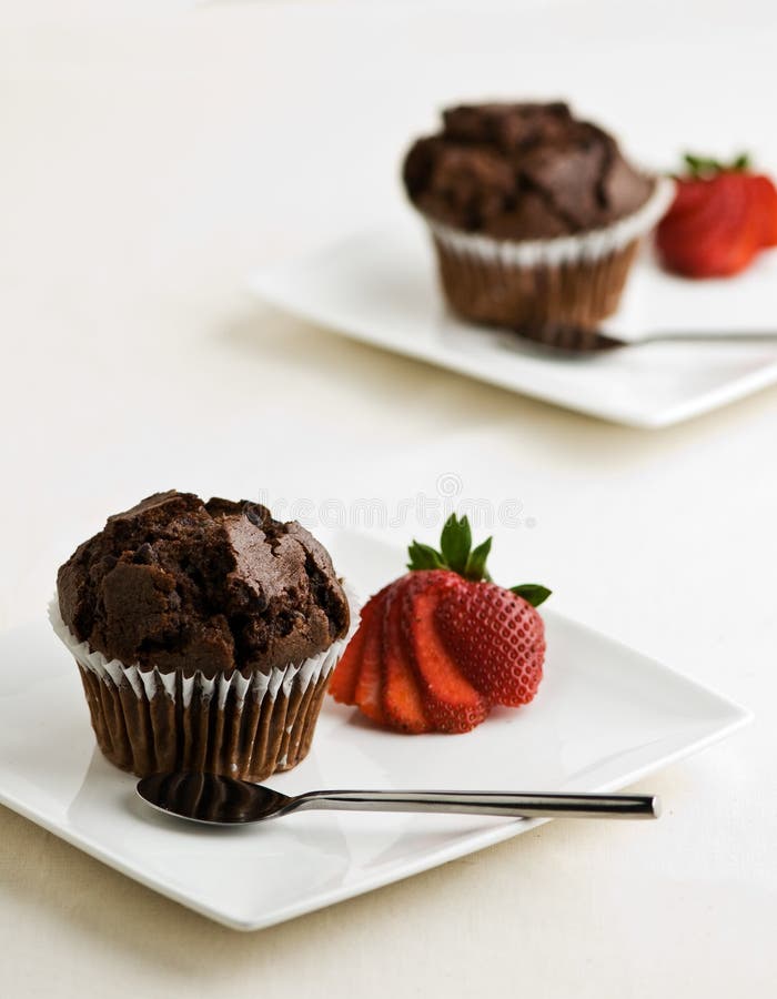 2 plates withchocolate muffins garnished with a strawberry. 2 plates withchocolate muffins garnished with a strawberry.