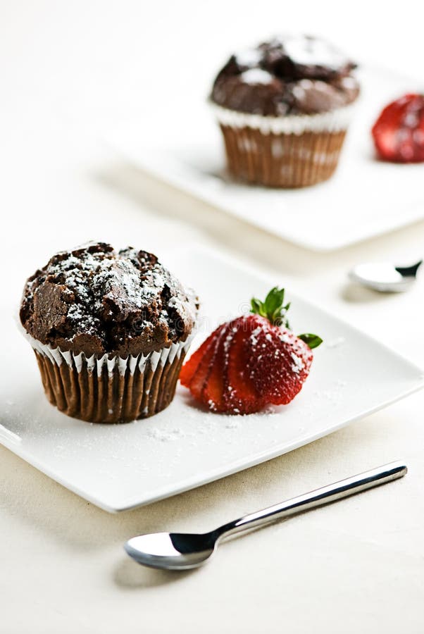 2 plates withchocolate muffins garnished with a strawberry. 2 plates withchocolate muffins garnished with a strawberry.