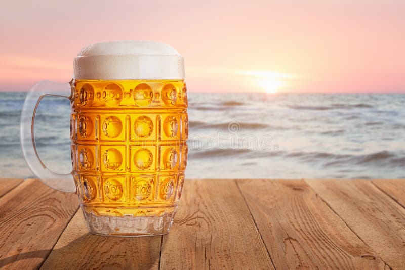 Mug of beer against sea on sunset