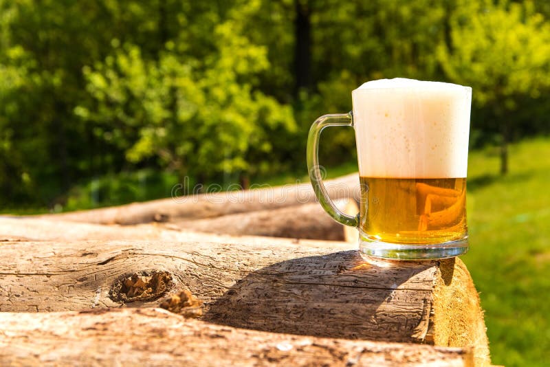 Mug with beer on a pile of logs near the forest. Beer in a glass. Cold refreshment in the countryside stock images
