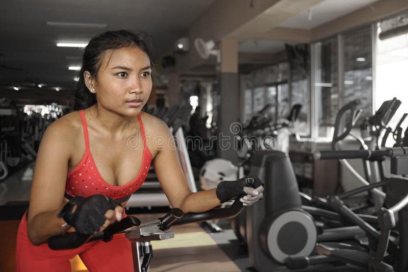Mujer activa asiática hermosa y sudorosa joven que entrena difícilmente al ciclo y a montar en entrenamiento estático de la bici fotos de archivo libres de regalías Mujer activa asiática hermosa y sudorosa joven que entrena difícilmente al ciclo y a montar en entrenamiento estático de la bici fotos de archivo libres de regalías