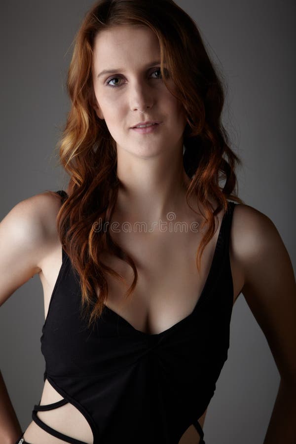 Young caucasian adult redhead woman with green eyes and very fair skin in a little black dress on a neutral grey background. Young caucasian adult redhead woman with green eyes and very fair skin in a little black dress on a neutral grey background