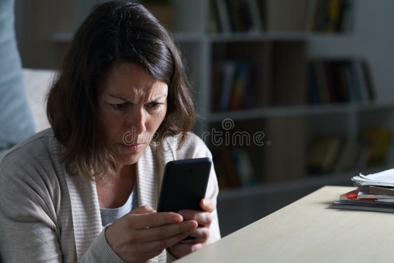 Mujer adulta preocupada leyendo noticias por teléfono en la noche en casa