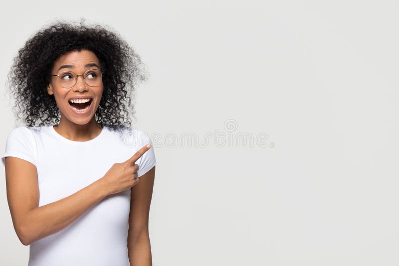 Mujer africana emocionada que mira para arriba a un lado punteaguda el finger en el copyspace