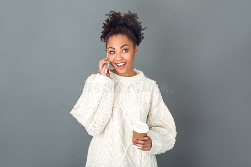 Mujer africana joven aislada en el concepto gris del invierno del estudio de la pared que habla con el amigo foto de archivo libre de regalías Mujer africana joven aislada en el concepto gris del invierno del estudio de la pared que habla con el amigo foto de archivo libre de regalías