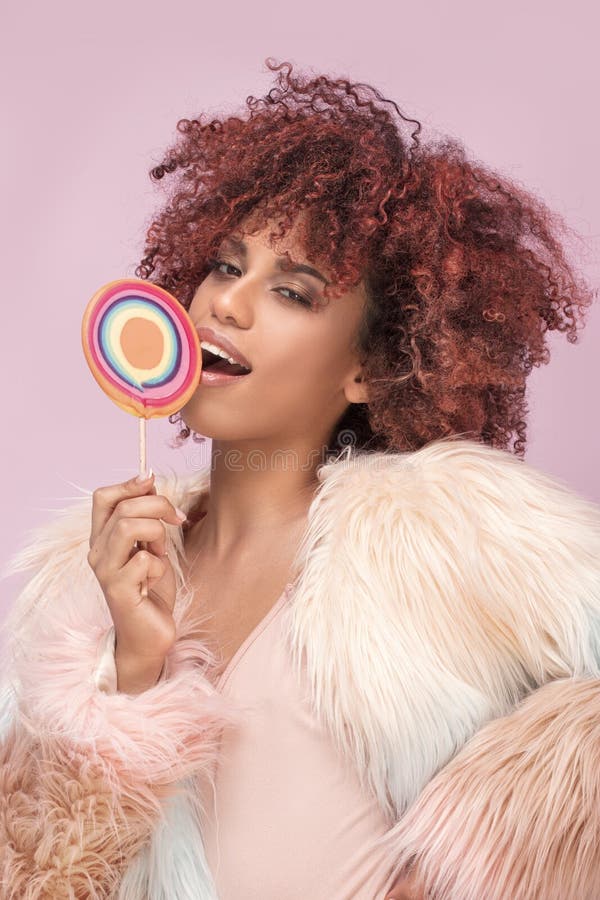 Mujer afro de moda con la piruleta en fondo rosado fotografía de archivo libre de regalías Mujer afro de moda con la piruleta en fondo rosado fotografía de archivo libre de regalías