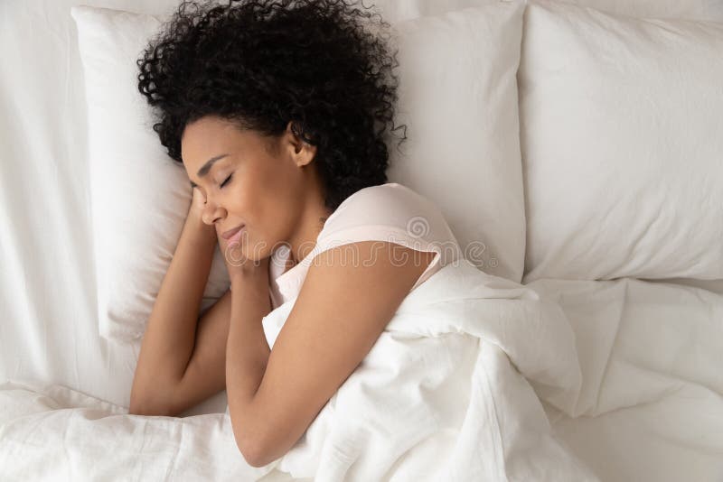Mujer afroamericana con las manos bajo la mejilla durmiendo en la cama