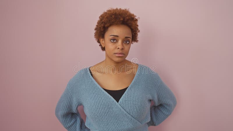 Mujer afroamericana con suéter azul posando sobre un fondo rosado en un retrato imágenes de archivo libres de regalías