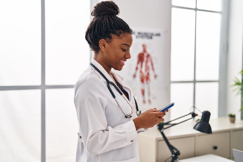 Mujer afroamericana con uniforme de médico usando smartphone trabajando en clínica