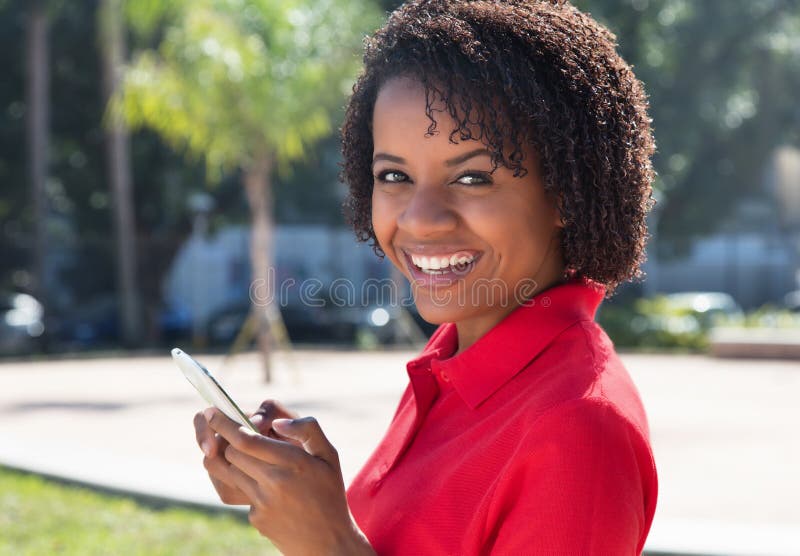 Mujer afroamericana de risa que envía el mensaje con el móvil fotografía de archivo libre de regalías Mujer afroamericana de risa que envía el mensaje con el móvil fotografía de archivo libre de regalías