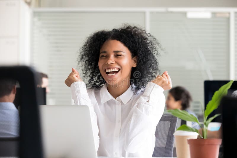 Mujer afroamericana emocionada que recibe buenas noticias en el ordenador portátil