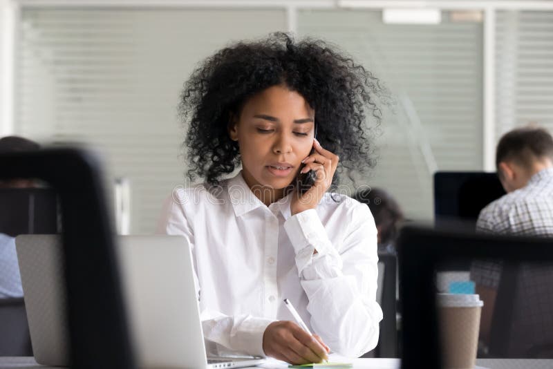 Mujer afroamericana enfocada que hace las notas, hablando en el teléfono imagenes de archivo Mujer afroamericana enfocada que hace las notas, hablando en el teléfono imagenes de archivo