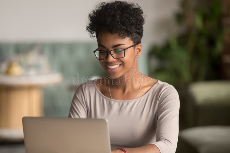 Mujer afroamericana feliz que usa estudio de trabajo del ordenador portátil en oficina Mujer afroamericana feliz que usa estudio de trabajo del ordenador portátil en oficina