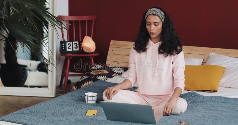 Mujer afroamericana joven hermosa que hace ejercicio de la yoga y que mira la lección preceptoral en el ordenador portátil en cas