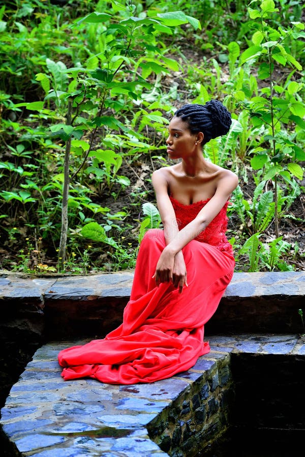 Mujer afroamericana que se sienta en un fondo de plantas verdes imagen de archivo libre de regalías Mujer afroamericana que se sienta en un fondo de plantas verdes imagen de archivo libre de regalías