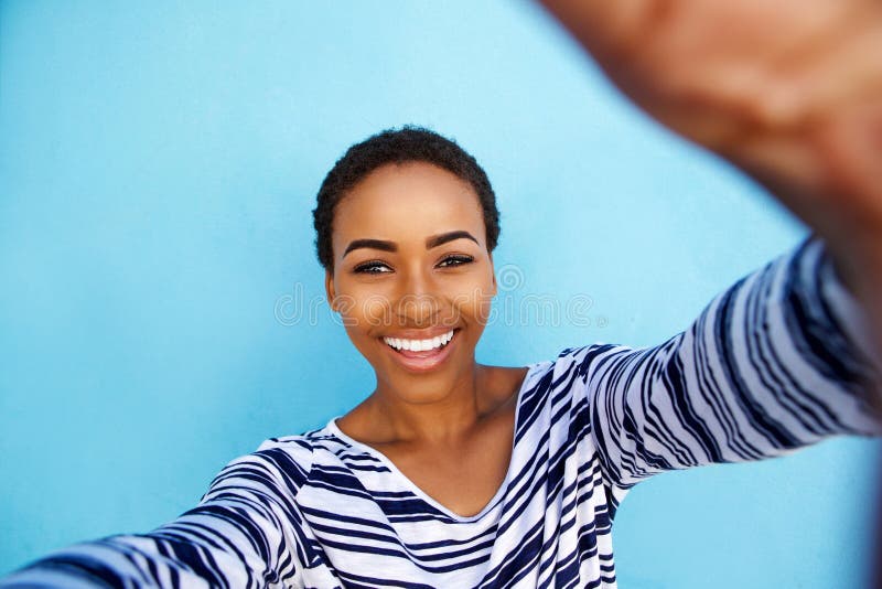 Mujer afroamericana sonriente que toma el selfie contra la pared azul imagen de archivo libre de regalías
