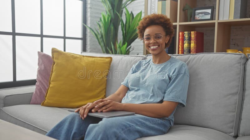 Mujer afroamericana sonriente relajándose en el sofá en un acogedor salón interior con decoración fotografía de archivo