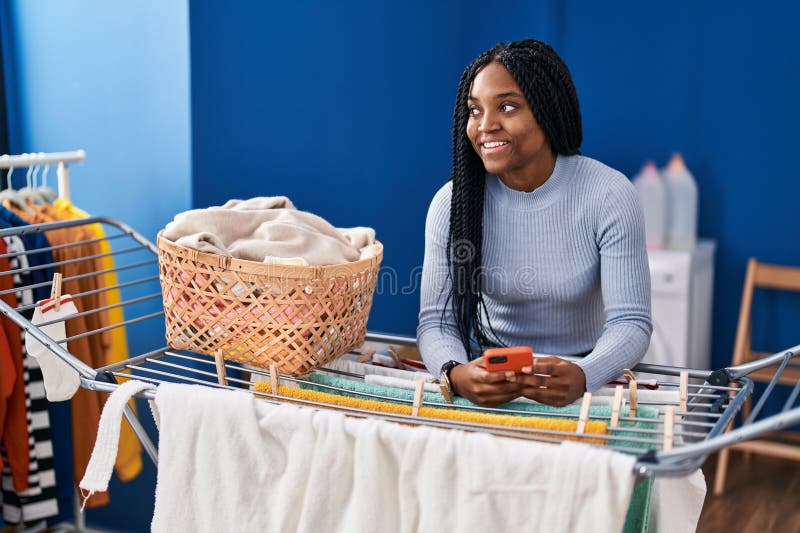 Mujer afroamericana usando un smartphone colgando ropa en la lavandería fotografía de archivo libre de regalías