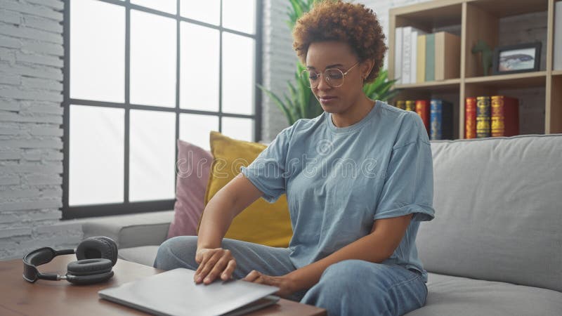 Mujer afroamericana vestida de forma casual, sentada con cuidado en un moderno salón interior imágenes de archivo libres de regalías