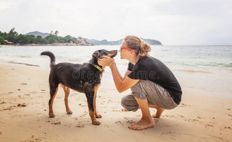 Mujer alegre feliz hermosa joven de la muchacha que se divierte con su perro en la playa descalzo en la arena fotos de archivo libres de regalías Mujer alegre feliz hermosa joven de la muchacha que se divierte con su perro en la playa descalzo en la arena fotos de archivo libres de regalías