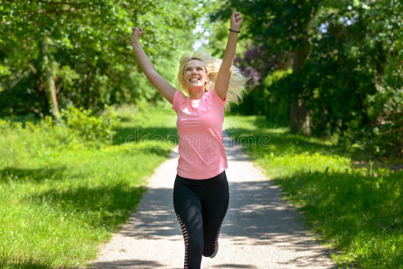 Mujer alegre que corre a lo largo de una pista del arbolado imágenes de archivo libres de regalías Mujer alegre que corre a lo largo de una pista del arbolado imágenes de archivo libres de regalías
