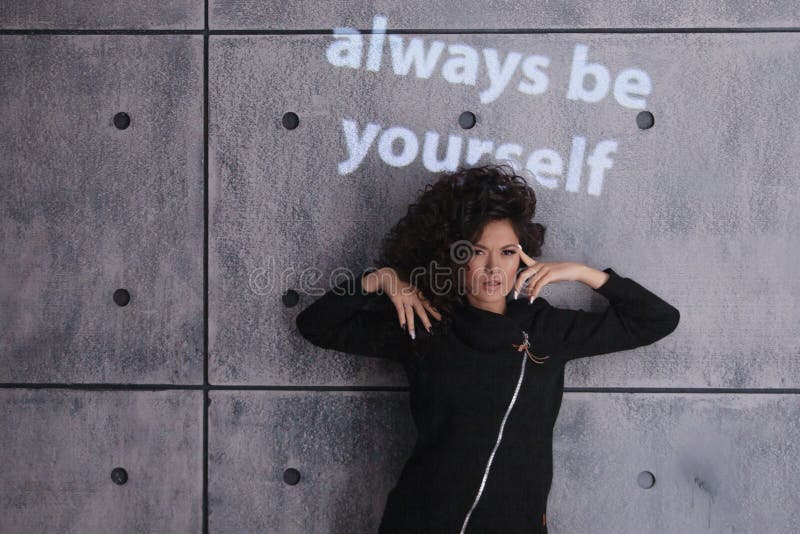 Mujer alegre y rizada bailando sobre un fondo de pared de concreto. InscripciÃ³n coloreada e iluminada dice: 'SÃ© siempre tÃº mism fotos de archivo
