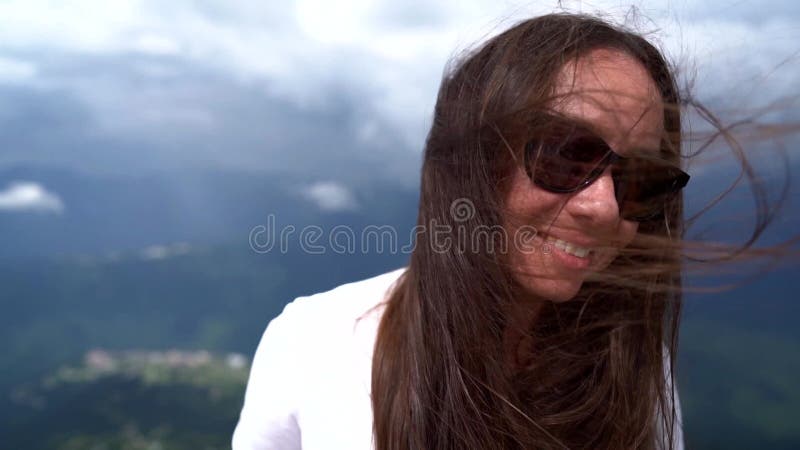 Mujer amante de la libertad feliz en la cima del vello largo oscuro de la montaña se balancea por el viento