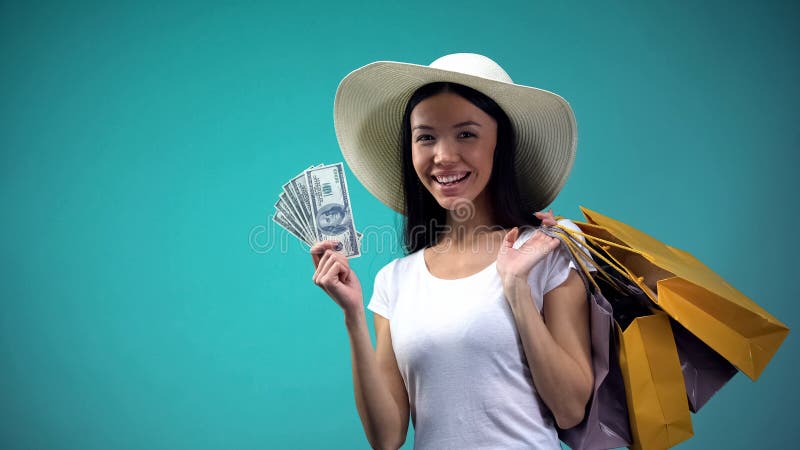 Mujer asi?tica en el sombrero del sol que lleva a cabo la suma grande de d?lares y de muchos bolsos que hacen compras, pr?stamo foto de archivo Mujer asi?tica en el sombrero del sol que lleva a cabo la suma grande de d?lares y de muchos bolsos que hacen compras, pr?stamo foto de archivo