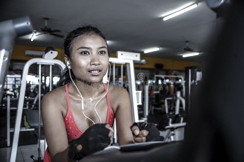 Mujer asiática atractiva y sudorosa que entrena difícilmente en el gimnasio usando el engranaje pedaling elíptico de la máquina e fotografía de archivo libre de regalías Mujer asiática atractiva y sudorosa que entrena difícilmente en el gimnasio usando el engranaje pedaling elíptico de la máquina e fotografía de archivo libre de regalías