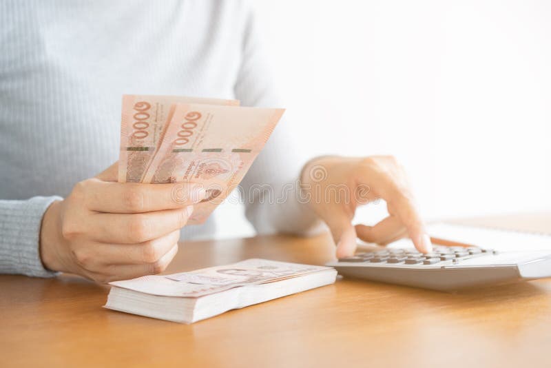Mujer asiática de la mano del primer usando la calculadora que cuenta y contar el dinero en hogar fotos de archivo Mujer asiática de la mano del primer usando la calculadora que cuenta y contar el dinero en hogar fotos de archivo