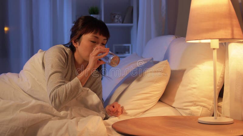 Mujer asiática despierta por la noche y toma de agua