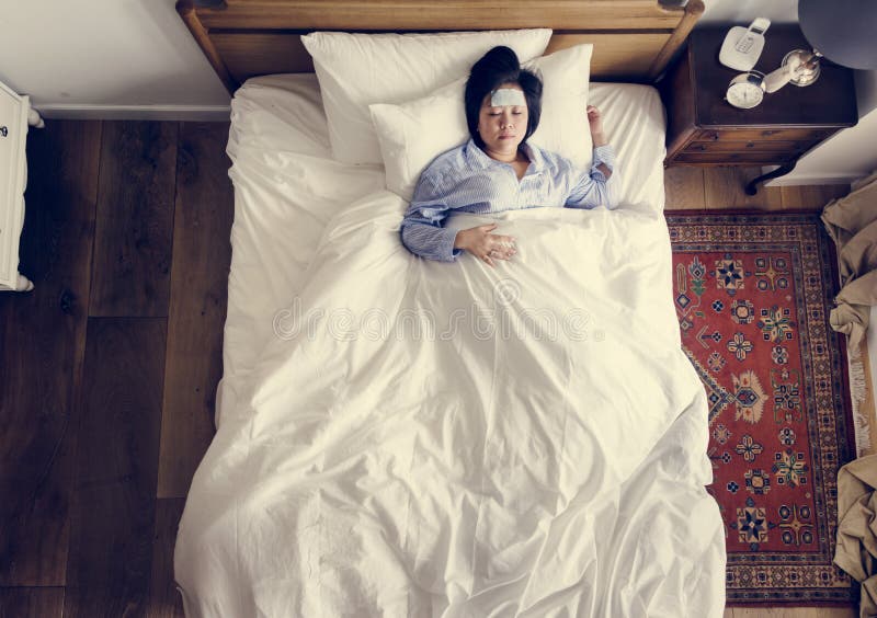 Mujer asiática enferma con fiebre que duerme en la cama imagen de archivo Mujer asiática enferma con fiebre que duerme en la cama imagen de archivo