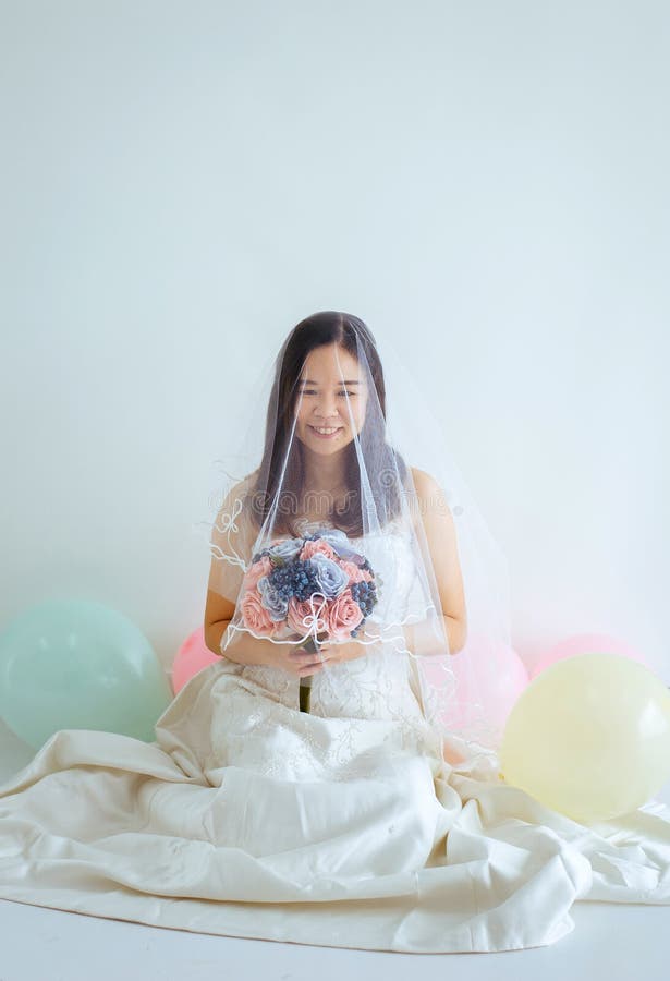 Mujer asiática hermosa de la novia en las manos blancas del vestido que sostienen la flor con la sensación feliz y divertida imagen de archivo Mujer asiática hermosa de la novia en las manos blancas del vestido que sostienen la flor con la sensación feliz y divertida imagen de archivo
