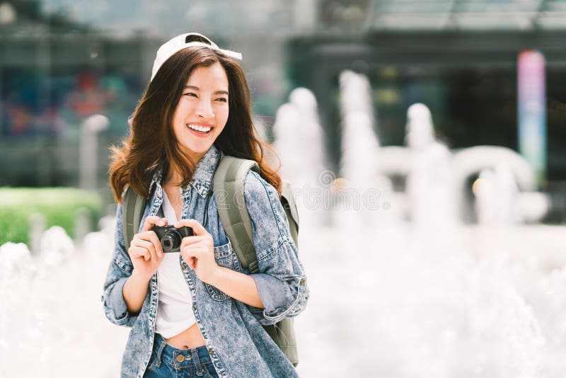 Mujer asiática hermosa joven del viajero de la mochila que usa la cámara compacta digital y la sonrisa, mirando el espacio de la