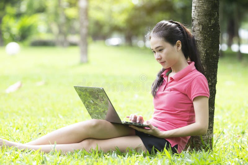 Mujer asiática hermosa que usa el ordenador portátil en el parque imágenes de archivo libres de regalías Mujer asiática hermosa que usa el ordenador portátil en el parque imágenes de archivo libres de regalías
