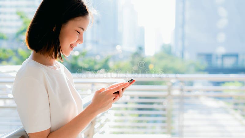 Mujer asiática hermosa que usa smartphone y la situación en el edificio de oficinas imágenes de archivo libres de regalías Mujer asiática hermosa que usa smartphone y la situación en el edificio de oficinas imágenes de archivo libres de regalías