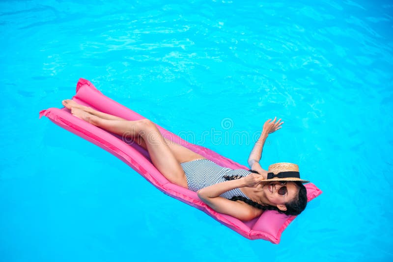 Mujer asiática joven con la cara de la cubierta del sombrero de paja que flota en el colchón inflable fotos de archivo libres de regalías Mujer asiática joven con la cara de la cubierta del sombrero de paja que flota en el colchón inflable fotos de archivo libres de regalías