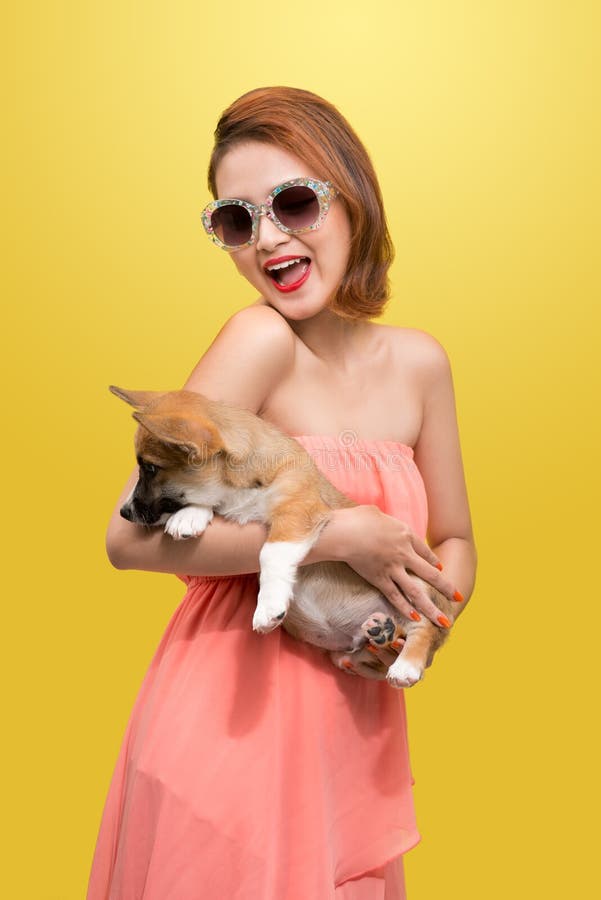Mujer asiática joven hermosa en el vestido agradable de la primavera, presentando en estudio con el perrito del corgi Foto de la fotografía de archivo Mujer asiática joven hermosa en el vestido agradable de la primavera, presentando en estudio con el perrito del corgi Foto de la fotografía de archivo