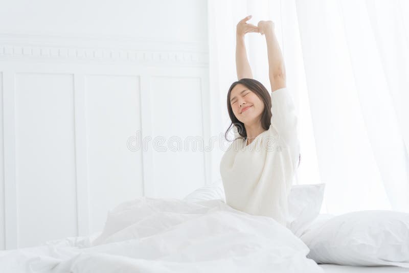 Mujer asiática joven por la mañana ella que estira en su cama en el dormitorio fotografía de archivo libre de regalías Mujer asiática joven por la mañana ella que estira en su cama en el dormitorio fotografía de archivo libre de regalías