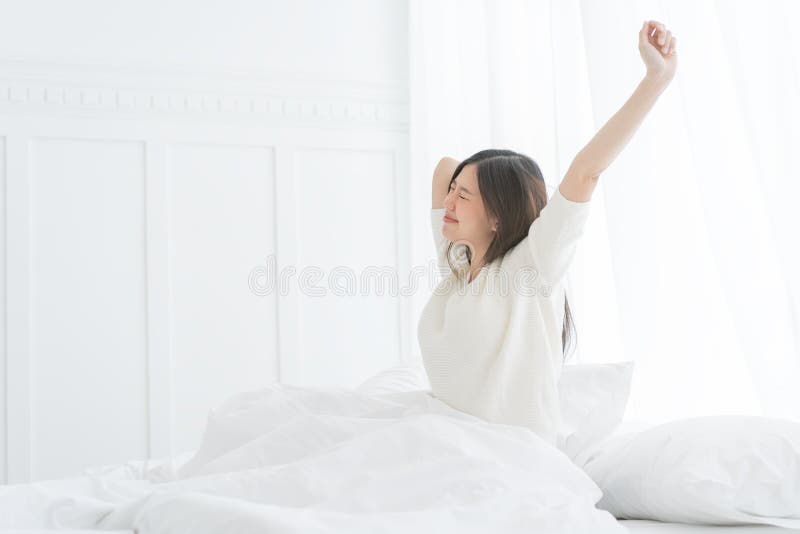 Mujer asiática joven por la mañana ella que estira en su cama en el dormitorio fotografía de archivo Mujer asiática joven por la mañana ella que estira en su cama en el dormitorio fotografía de archivo