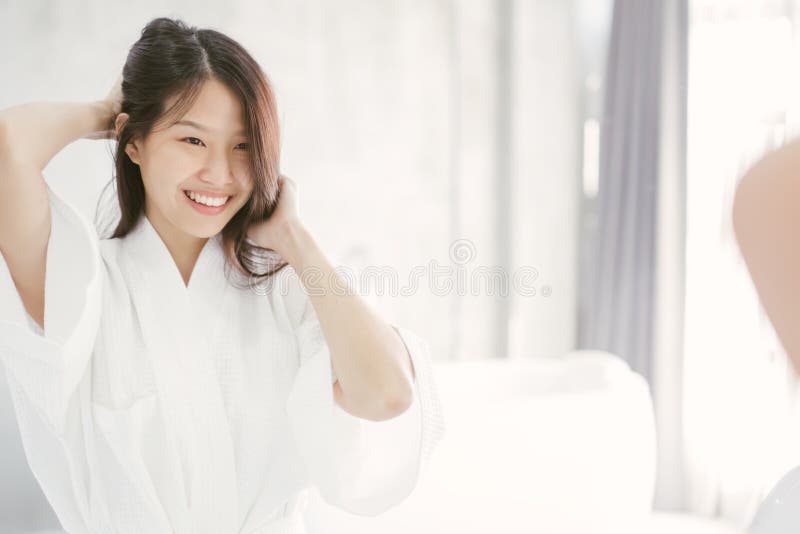 Mujer asiática joven que mira su cara en espejo en cuarto de baño imagen de archivo Mujer asiática joven que mira su cara en espejo en cuarto de baño imagen de archivo