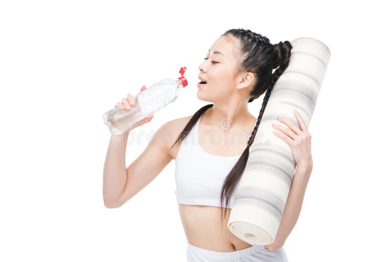 Mujer asiática joven que sostiene la estera de la yoga y el agua potable de la botella foto de archivo libre de regalías Mujer asiática joven que sostiene la estera de la yoga y el agua potable de la botella foto de archivo libre de regalías