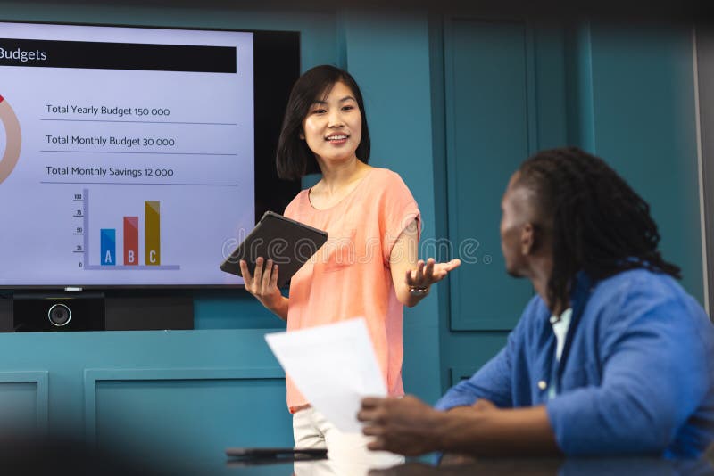 Asian woman presenting, African American man listening in a modern business office. She has black hair, he has dreadlocks; both are young and wearing casual clothes, unaltered. Asian woman presenting, African American man listening in a modern business office. She has black hair, he has dreadlocks; both are young and wearing casual clothes, unaltered.