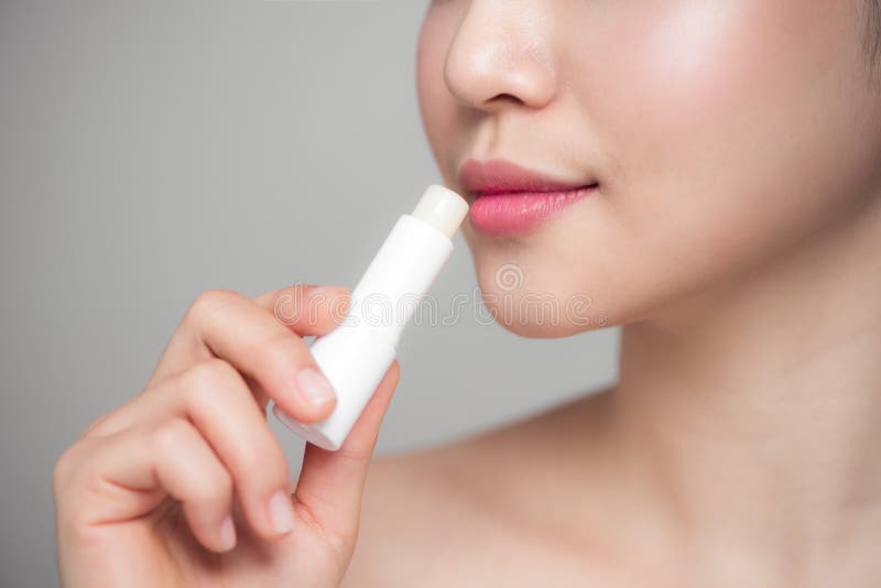 Mujer asiática que aplica protector labial higiénico sobre fondo gris fotografía de archivo Mujer asiática que aplica protector labial higiénico sobre fondo gris fotografía de archivo