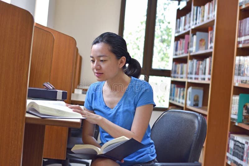 Mujer asiática que hace el libro de la investigación y de lectura en biblioteca imagenes de archivo