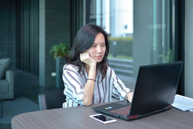 Mujer asiática subrayada del negocio casual que usa un ordenador portátil en la propiedad horizontal, GE imágenes de archivo libres de regalías Mujer asiática subrayada del negocio casual que usa un ordenador portátil en la propiedad horizontal, GE imágenes de archivo libres de regalías