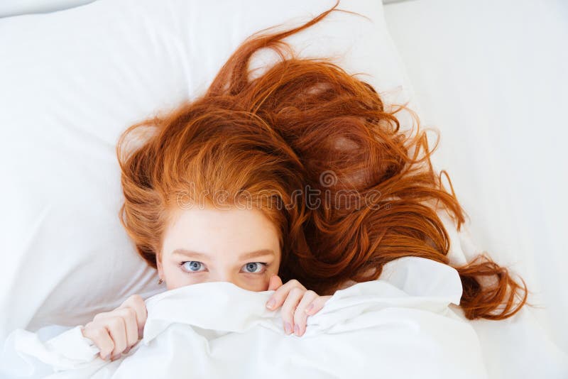 Mujer asustada que miente en cama y que oculta debajo de la hoja imagen de archivo libre de regalías Mujer asustada que miente en cama y que oculta debajo de la hoja imagen de archivo libre de regalías