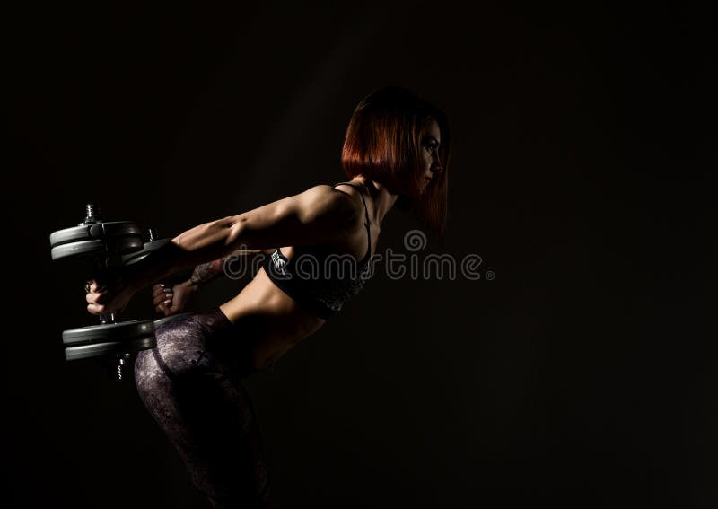 Mujer atlética joven en ropa de deportes con un dumbbellson un fondo oscuro Espacio libre para el texto imagen de archivo libre de regalías Mujer atlética joven en ropa de deportes con un dumbbellson un fondo oscuro Espacio libre para el texto imagen de archivo libre de regalías