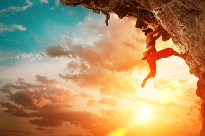 Mujer atlética que sube en roca sobresaliente del acantilado con el fondo del cielo de la puesta del sol